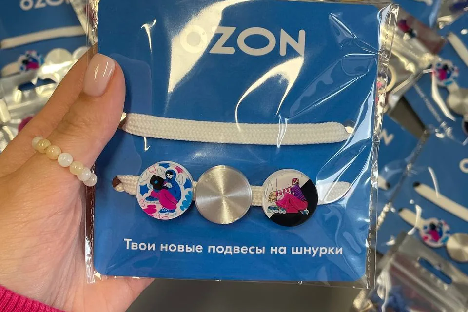 Подвесы на шнурки в синей фирменной упаковке Ozon в руке, на фоне — тираж таких же