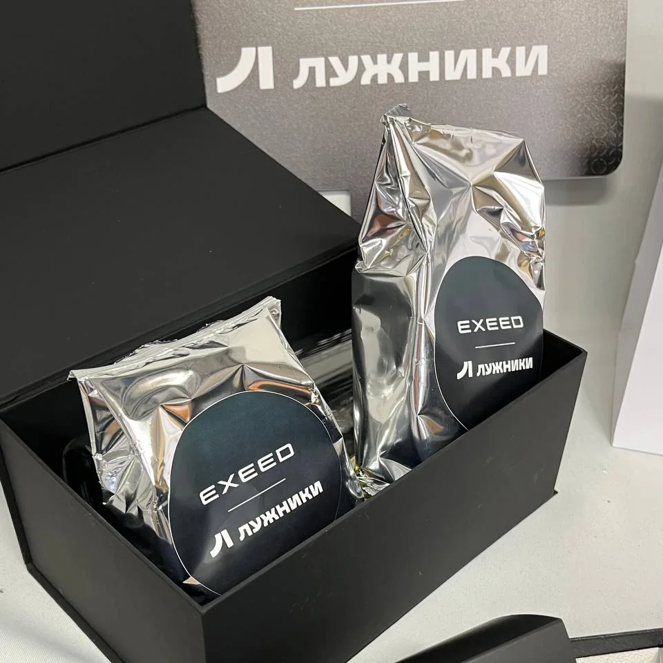 Открытая чёрная подарочная коробка с двумя фольгированными пакетами с наклейками EXEED и «Лужники»